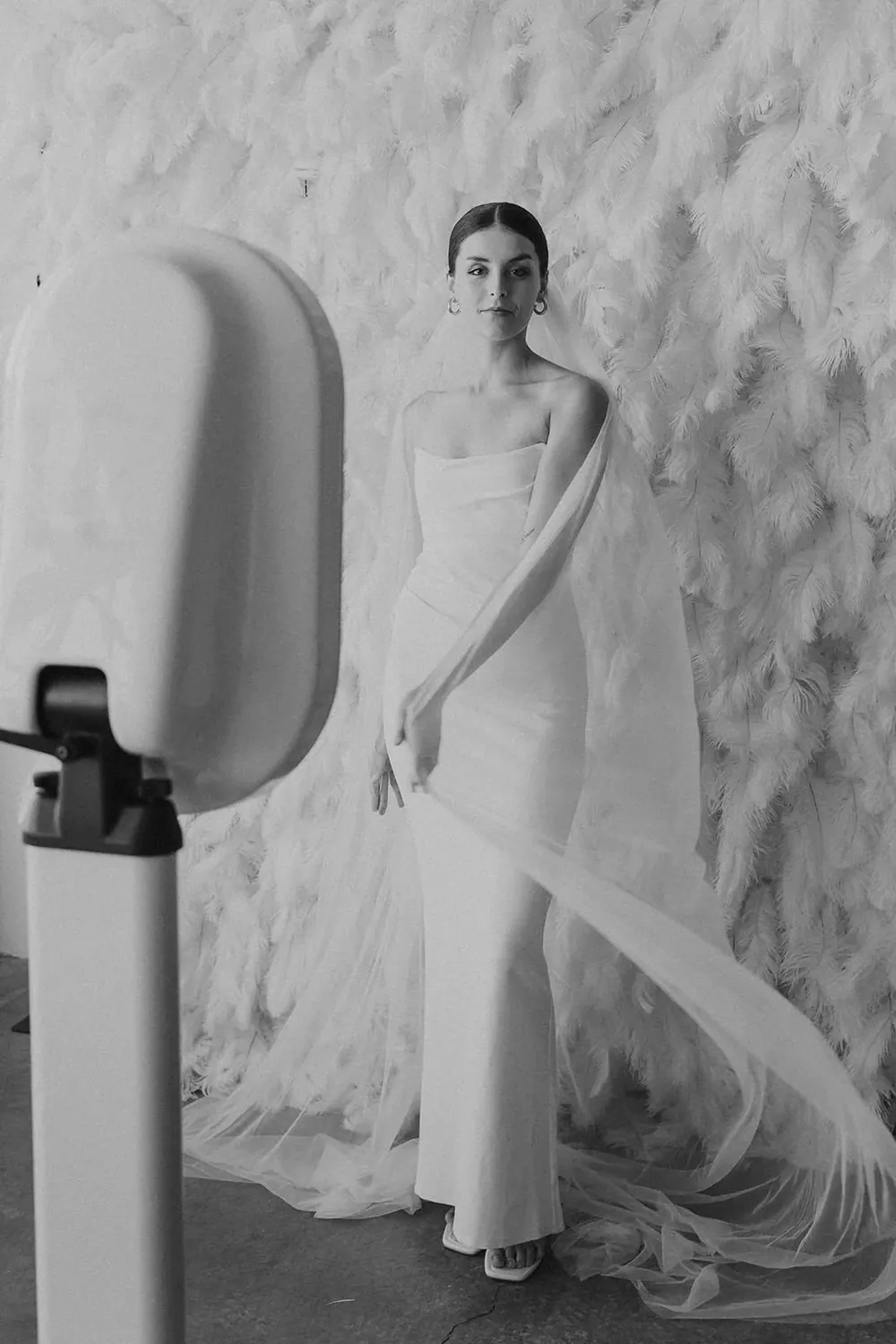 Guest in white posing in front of a white textured flower wall beside a photo booth