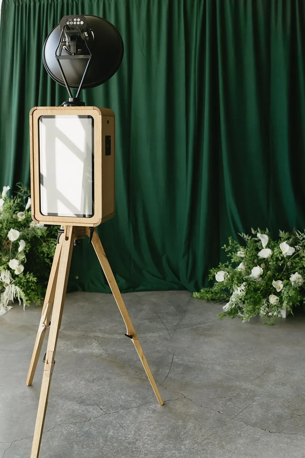 Photo booth on a wooden stand in front of a draped backdrop with florals