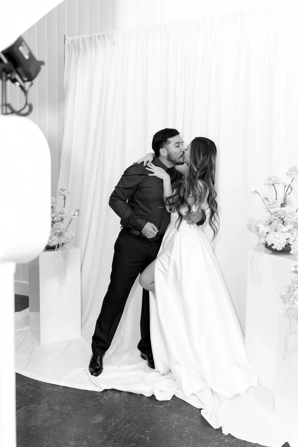 Black and white photo of a couple embracing in front of a white draped backdrop.