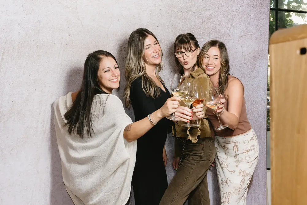 Four guests raising their glasses together in front of a pale wall.