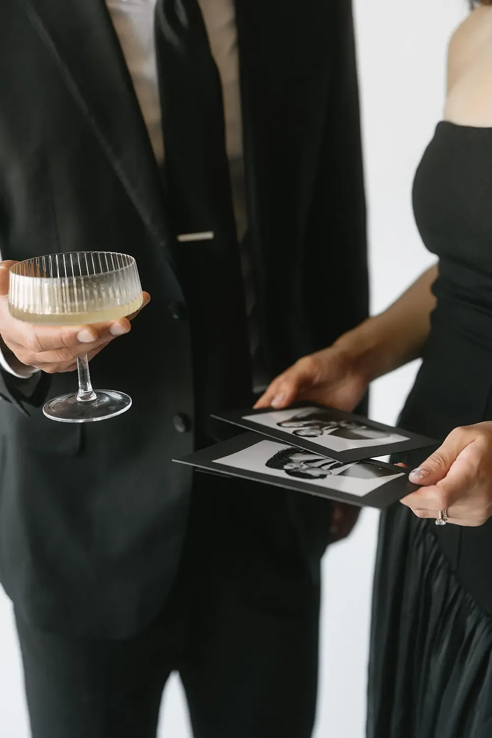 Two guests holding freshly printed black and white photos beside a champagne coupe.