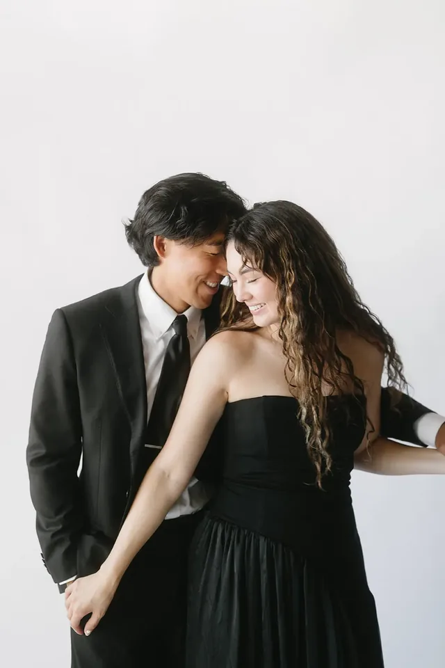 Couple in black formalwear posing against a bright white studio backdrop.