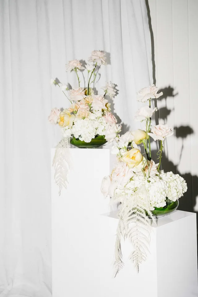 Pale floral arrangement styled against a white drapery backdrop