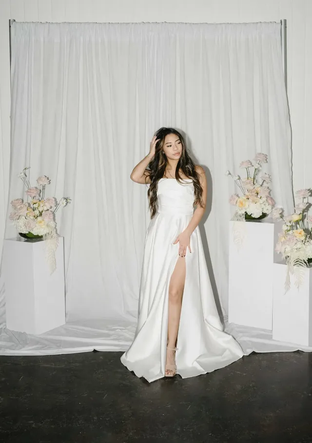 Guest in a white gown standing in front of a white drapery backdrop with florals