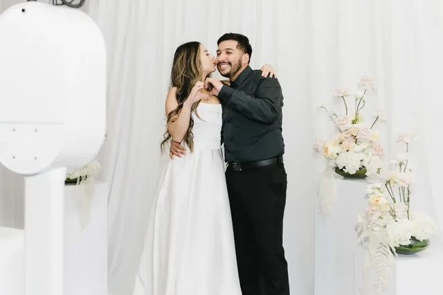 Couple posing beside a white open-air photo booth surrounded by floral styling.