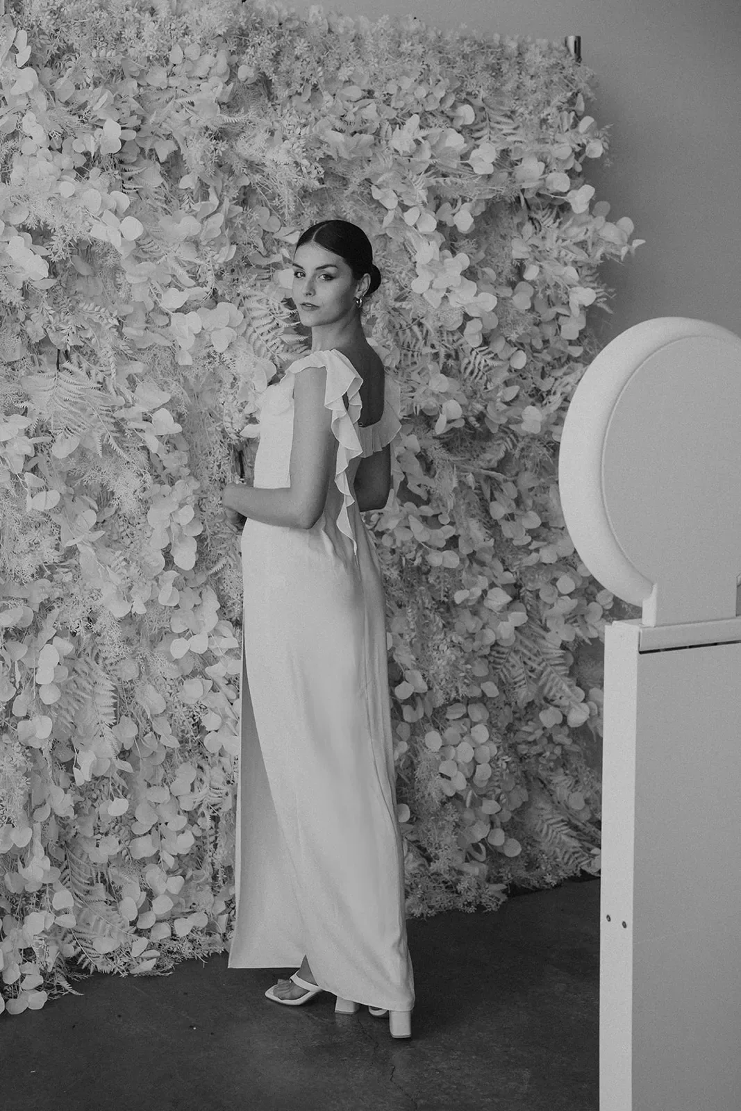 Guest posing in front of a white textured flower wall beside an open-air photo booth.