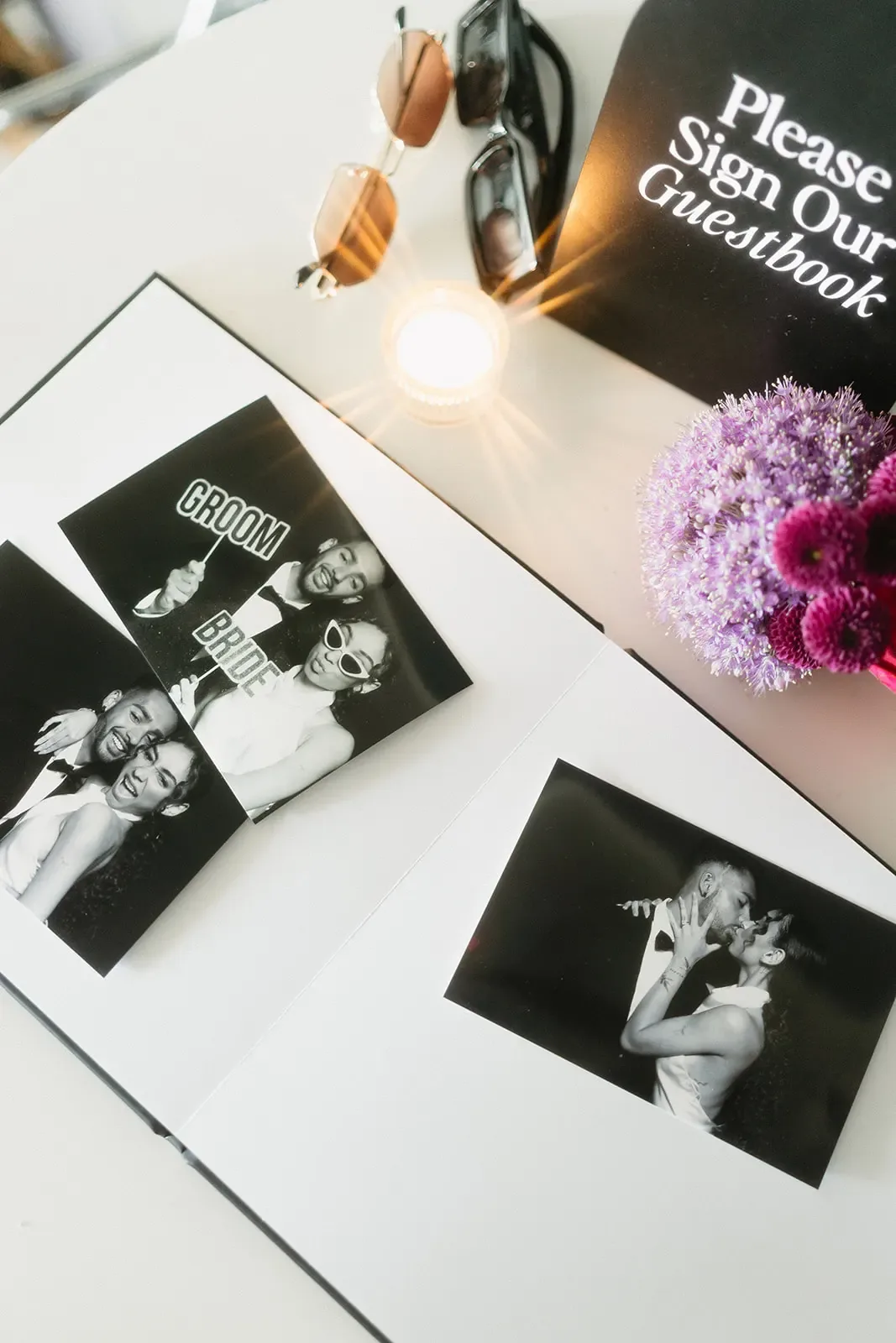 Keepsake album open beside a printed event sign, photo prints and florals.
