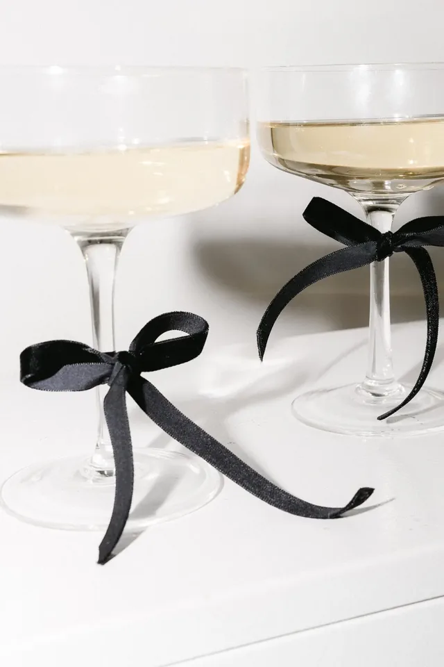 Two coupe glasses tied with black ribbon bows on a white table.