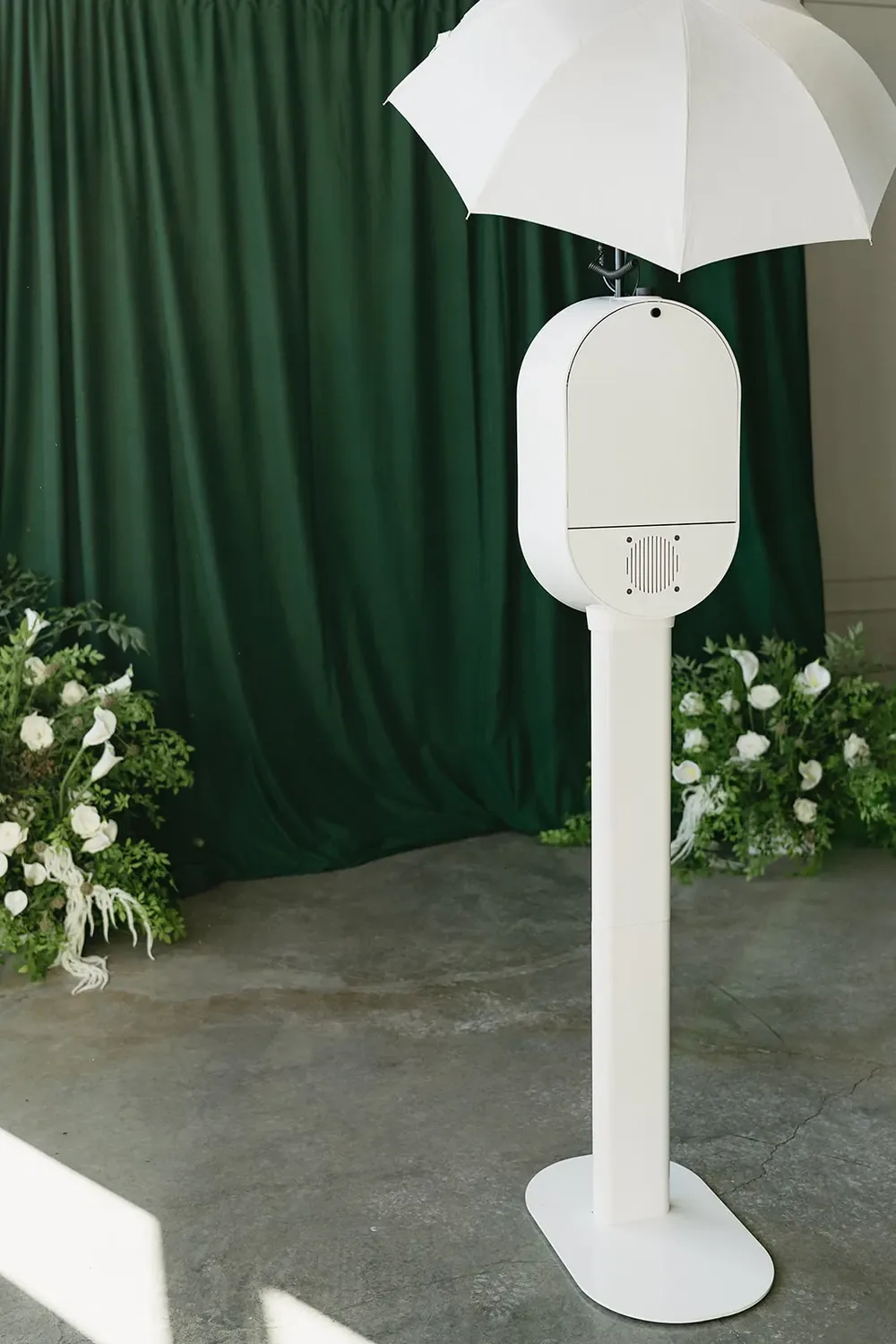 Open-air photo booth on a stand beside a draped backdrop and florals