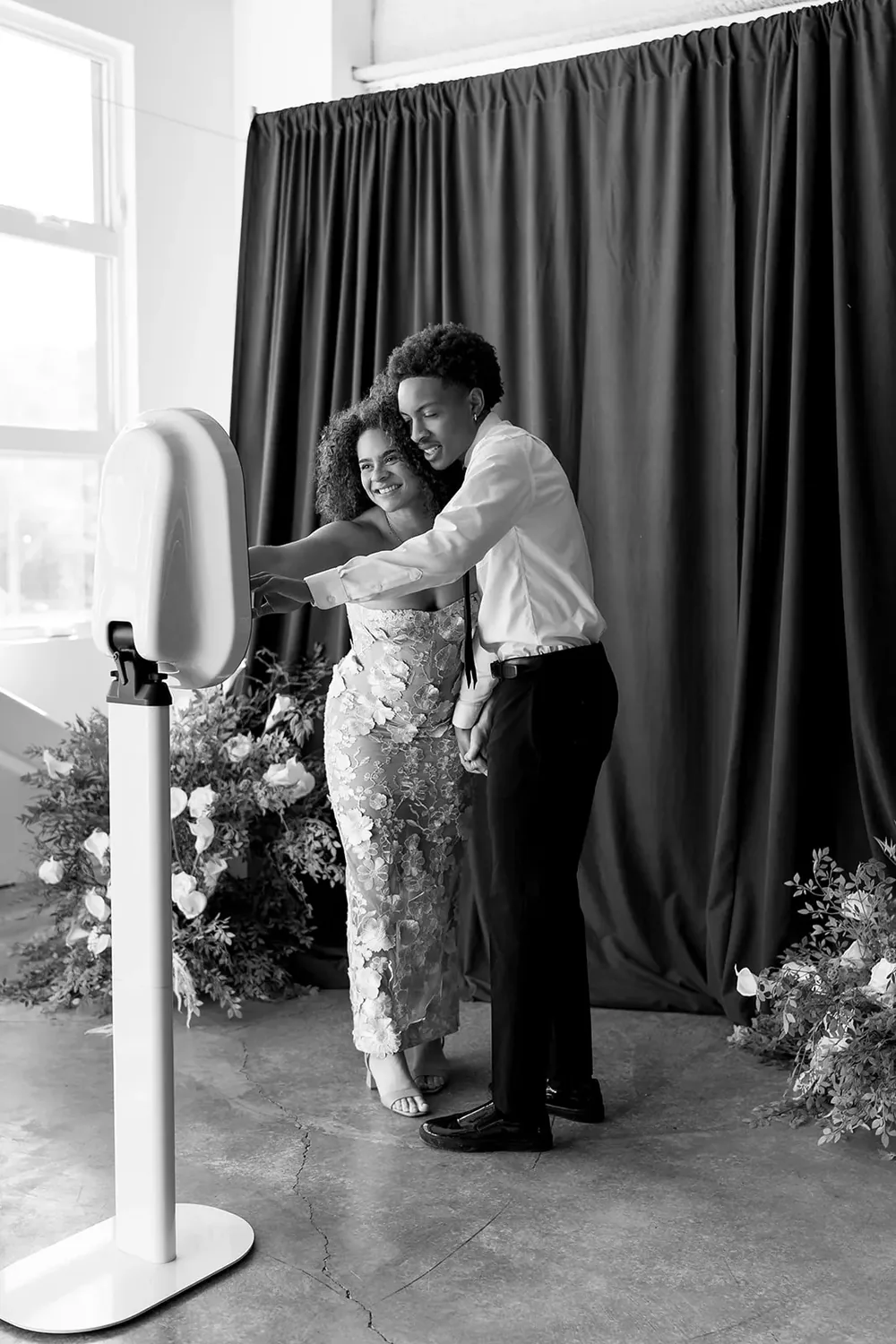 Guests stepping into the open-air booth beside a draped backdrop with florals