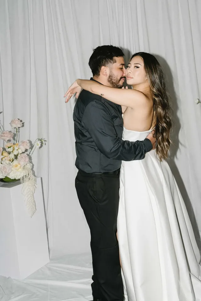Couple embracing in front of a white drapery backdrop with soft florals