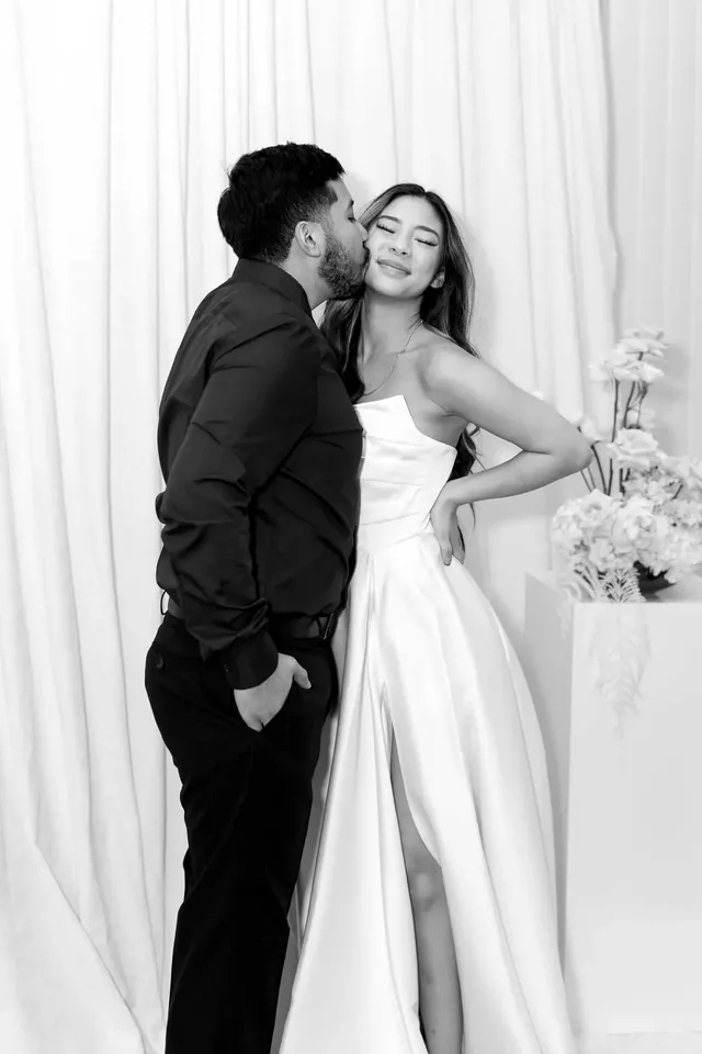 Black and white photograph of a couple leaning together in front of draped fabric