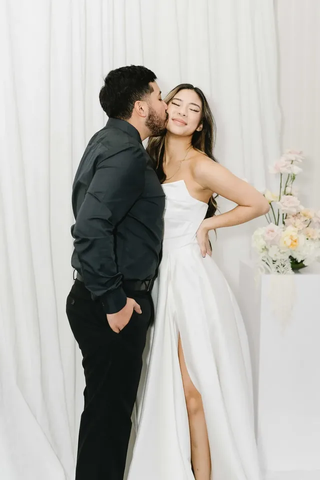 Couple posing together against a white draped backdrop with florals