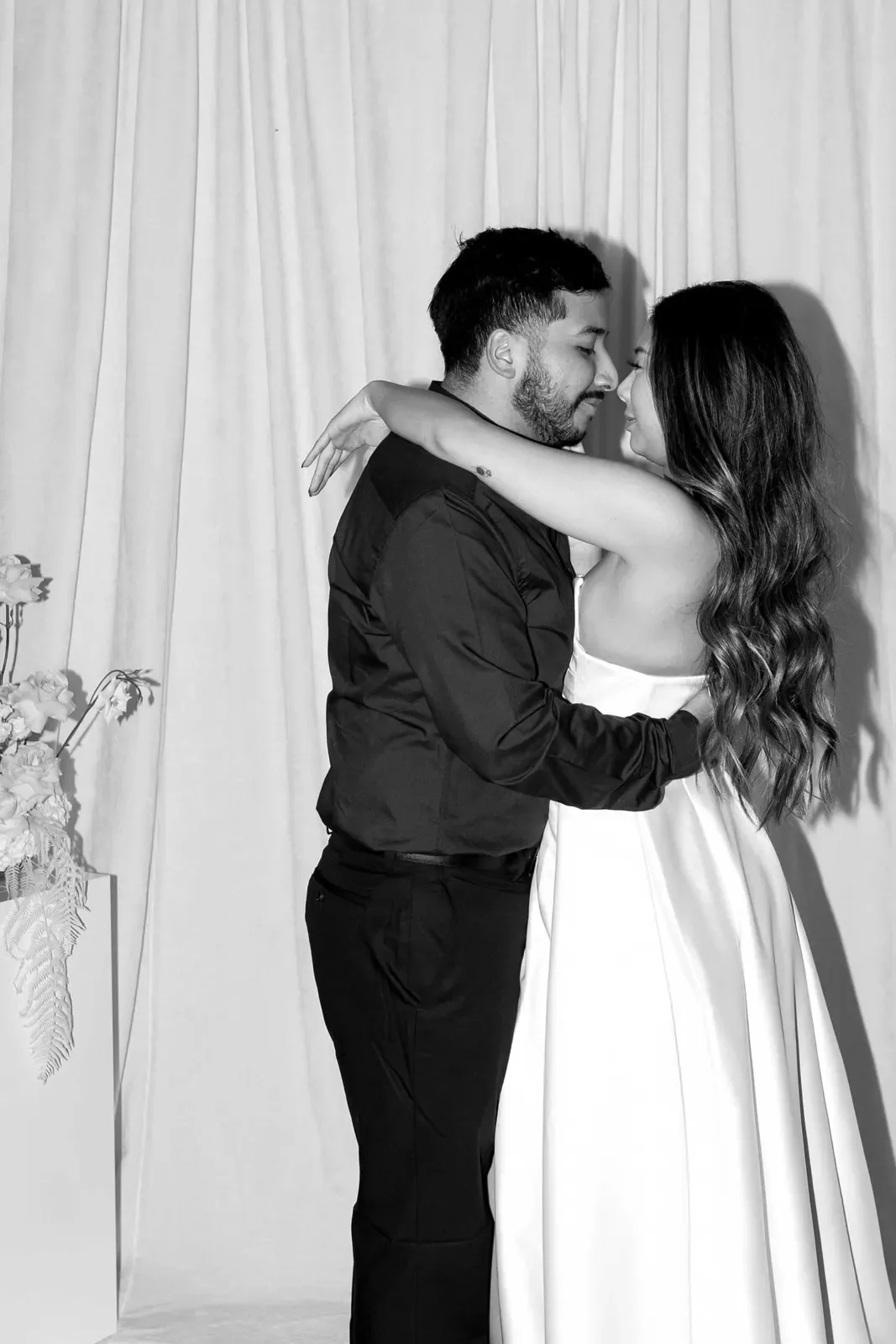 Black and white photograph of a couple embracing beside draped fabric