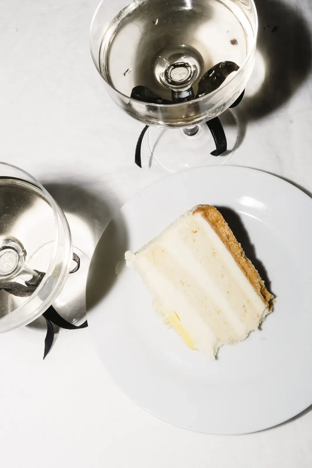 Slice of cake and a ribbon-tied coupe glass on a white table