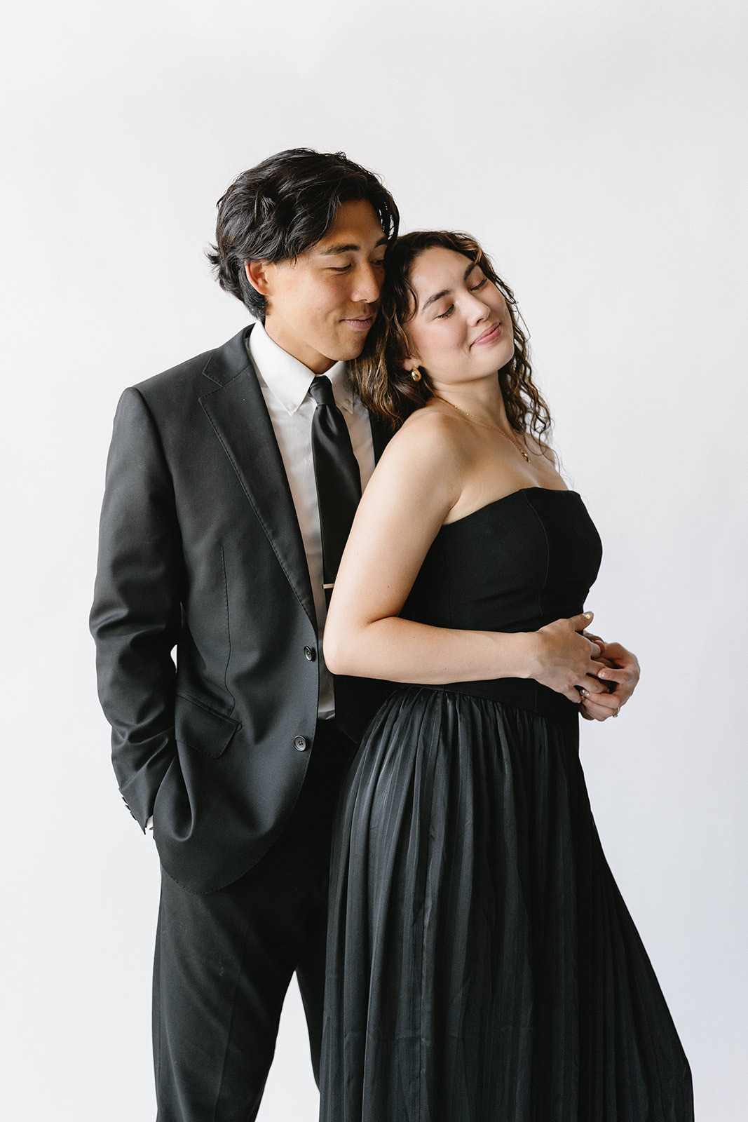 Couple in formalwear photographed against a plain white studio backdrop.