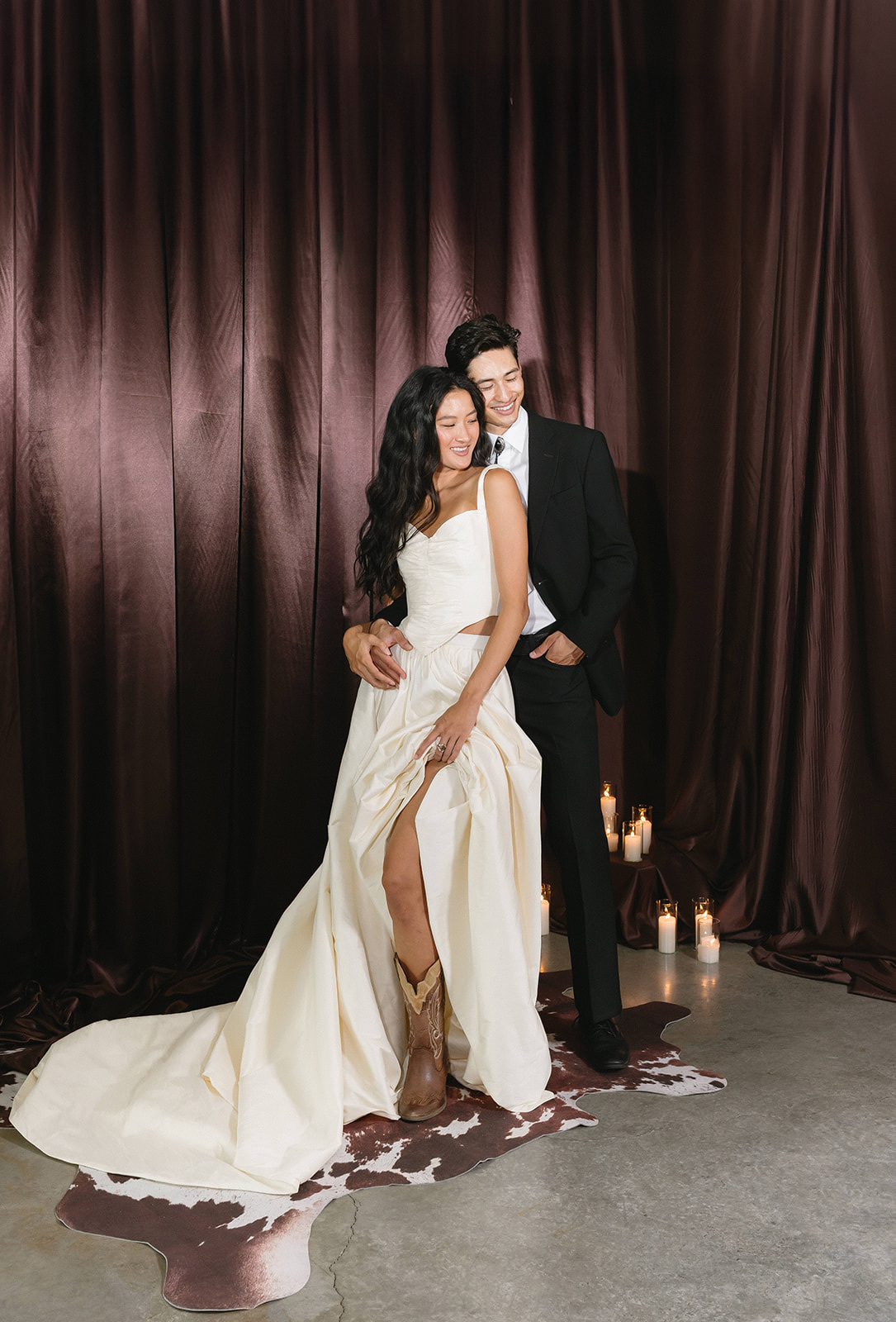 Couple standing in front of a floor-length draped fabric backdrop lit with candles.